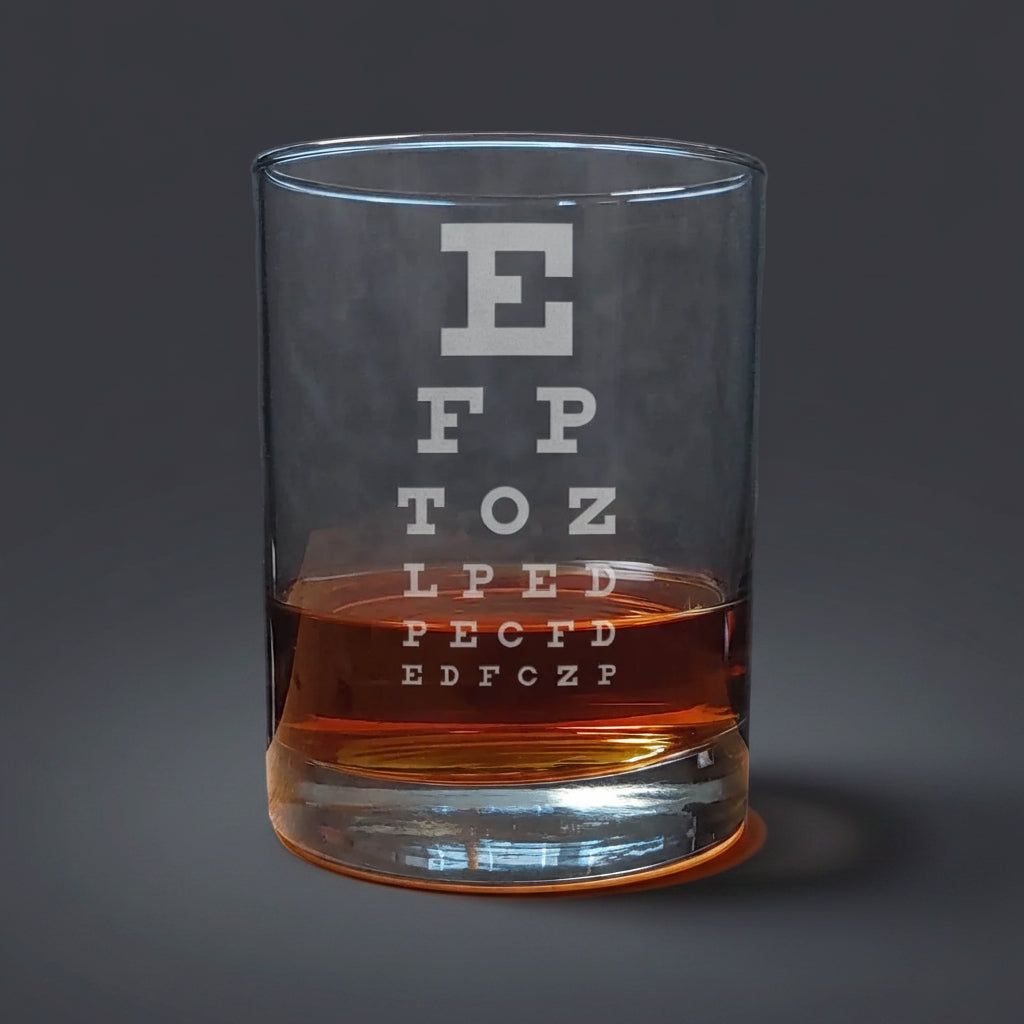 Clear glass tumbler with an eye test chart etched on it, filled with a brown liquid, on a wooden surface.