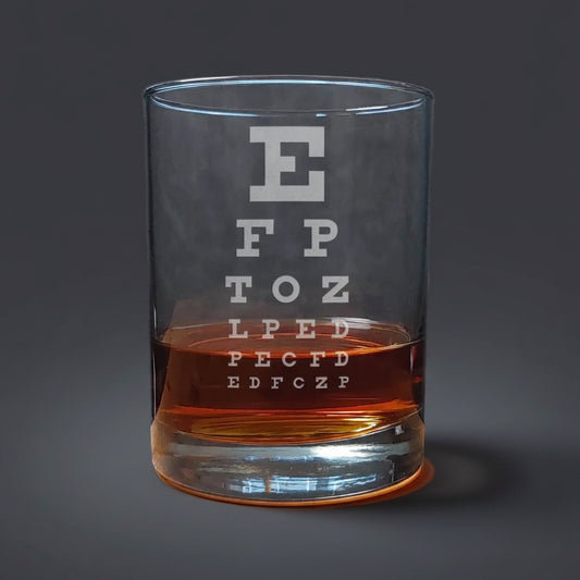 Clear glass tumbler with an eye test chart etched on it, filled with a brown liquid, on a wooden surface.