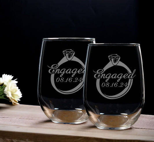 A set of 2 Stemless Wine Glasses with the image of an engagement ring with the word "Engaged"and the date across the ring. - Copyright Hues in Glass