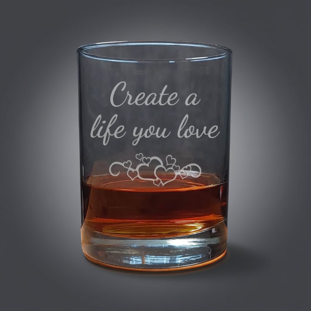 Clear glass tumbler with engraved text "Create a life you love and hearts on a wooden surface.