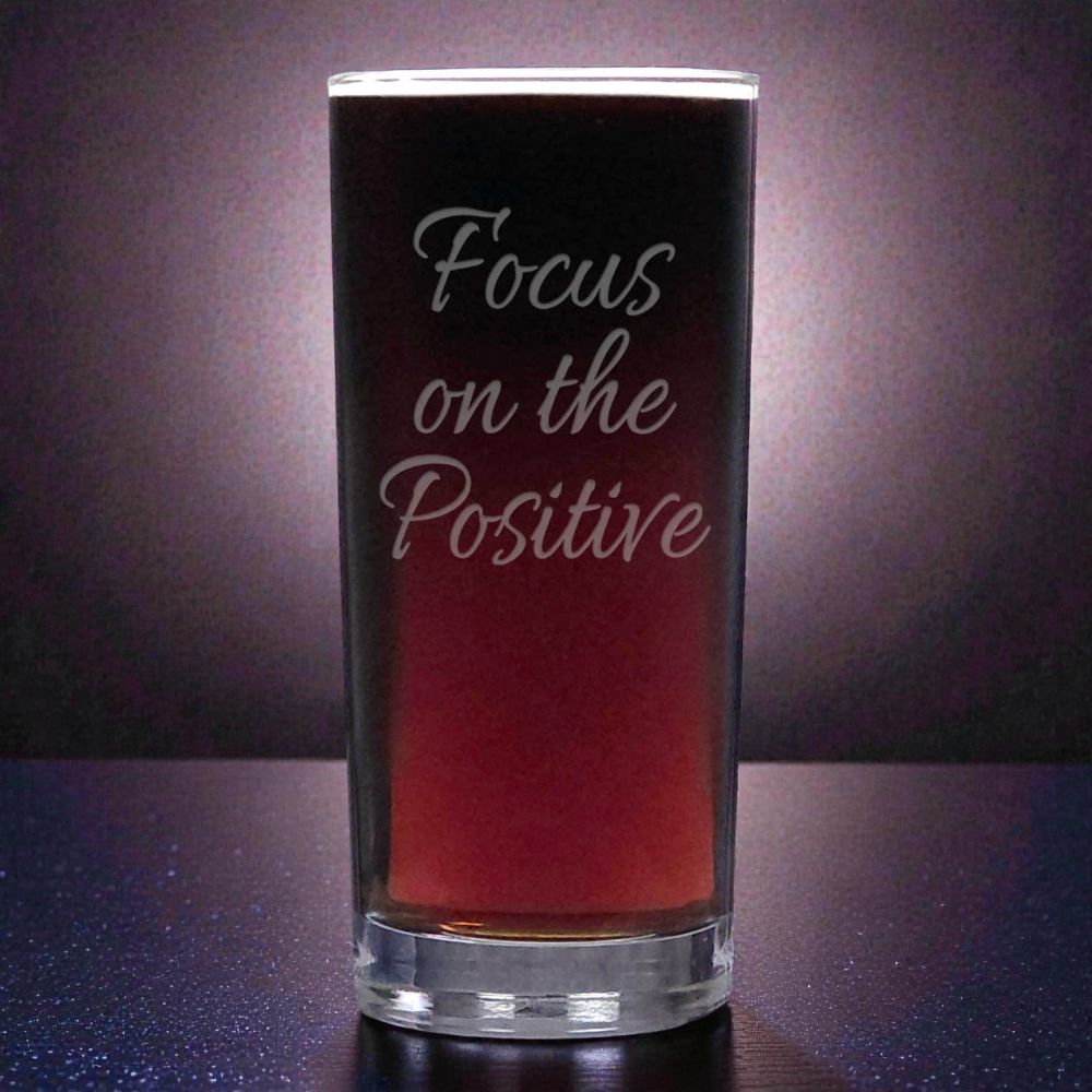 Glass with 'Focus on the Positive' text against a dark background