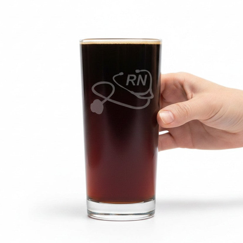 A hand holding a tall clear glass filled with dark beverage, featuring an etched graphic of a stethoscope and the letters 'RN'.