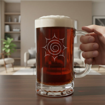 A hand holds a large clear glass beer mug filled with amber beer and topped with white foam, with an etched spiral sun design set on a wooden table in a softly blurred living room background.