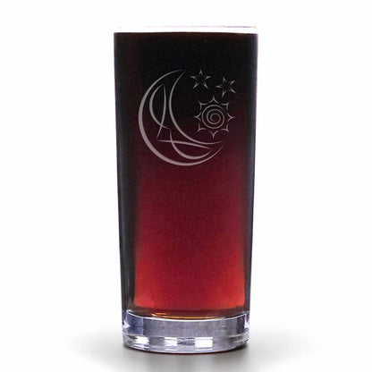 A clear glass shot glass with a gradient tint from dark brown to deep red, featuring an etched crescent moon, sun, and stars design on the front, set against a plain white background.