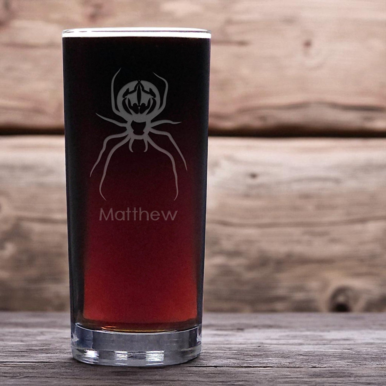 Cooler glass with spider design and 'Matthew' text on a wooden background
