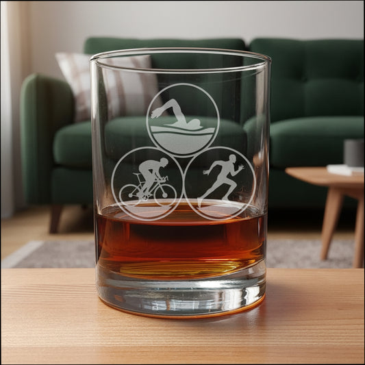 Glass tumbler with Triathlon symbols filled with a brown liquid on a wooden surface.