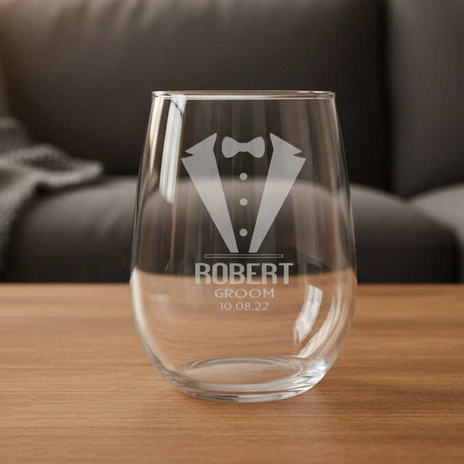Clear glass with engraved tuxedo design and text on a wooden surface with black couch in backgroundi