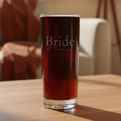 Cooler glass filled with red liquid and etched with the word 'Bride' with a living room in the 
background