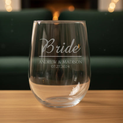 Clear glass wine glass engraved with 'Bride' and personalized text on a wooden surface with a green couch in the background