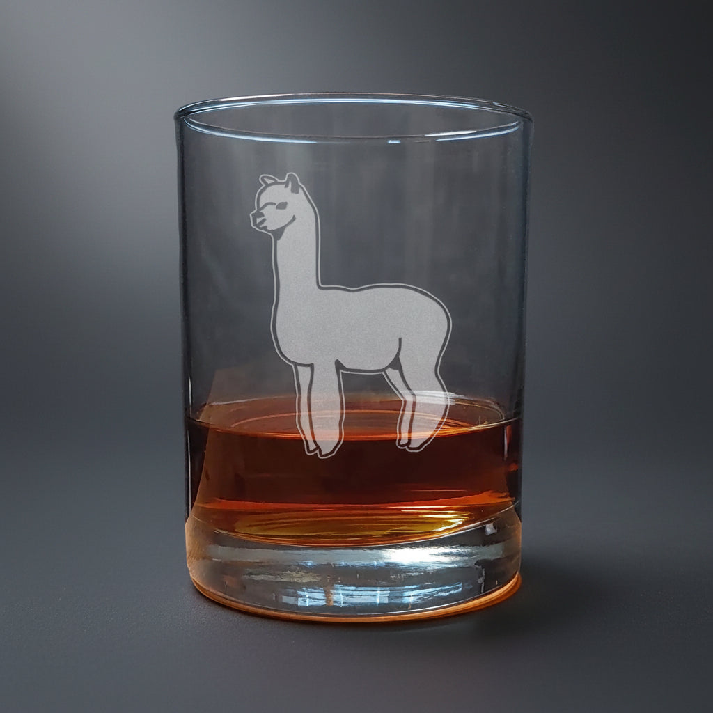 Clear glass tumbler with a llama design filled with amber liquid on a wooden surface.