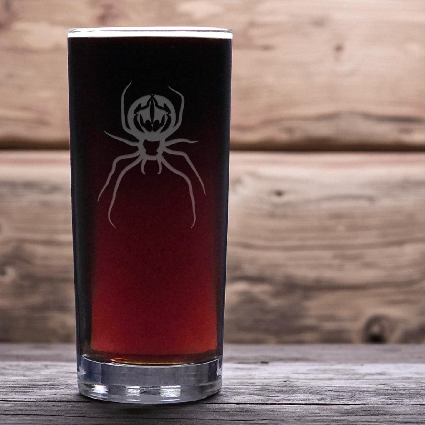 Cooler glass with spider design filled with dark liquid on a wooden surface